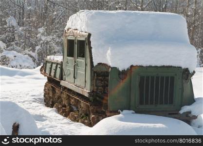Old broken chain tractor covered with snow in the woods