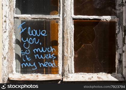 Old broken grunge part of weathered window of abandoned house with funny graffiti notice on glass