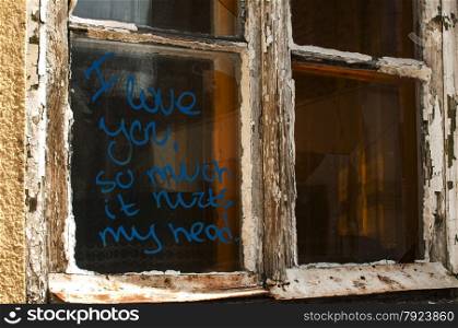 Old broken grunge part of weathered window of abandoned house with funny graffiti notice on glass