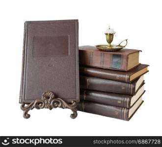 Old brown hardcover books and burning candle in antique copper candlestick isolated on white background, with copy-space