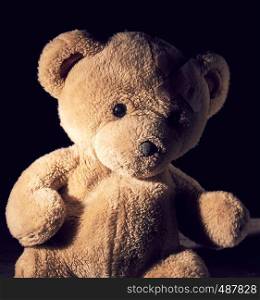 old brown teddy bear is sitting , plaster is glued on his forehead, black background