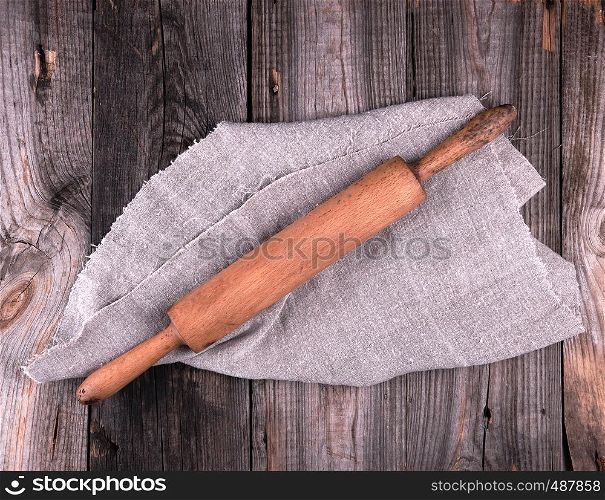 old brown wooden rolling pin on a gray linen napkin, top view