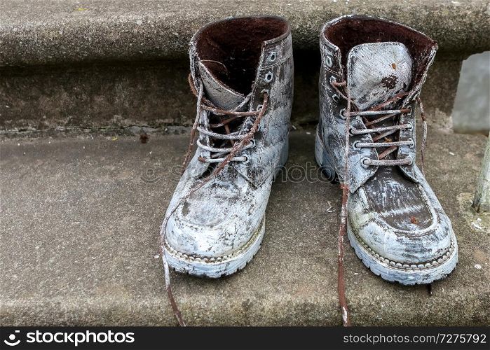 Old brown work boots. Boots smeared with white paint. Dirty boots on the stairs. Dirty old workboots on stairs.
