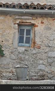 Old bucket above draw well in front of old building with lattice window.