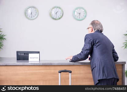 Old businessman at the hotel reception in business travel concept. Old businessman at the hotel reception