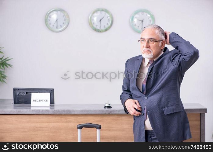 Old businessman at the hotel reception in business travel concept. Old businessman at the hotel reception
