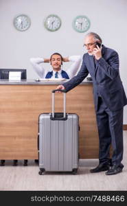 Old businessman at the hotel reception in business travel concept. Old businessman at the hotel reception