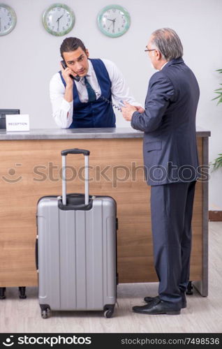 Old businessman at the hotel reception in business travel concept. Old businessman at the hotel reception