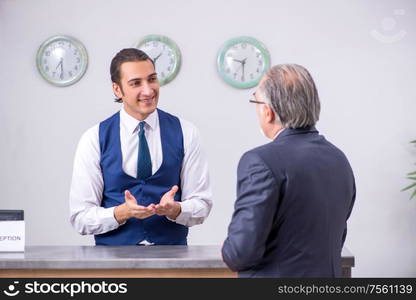 Old businessman at the hotel reception in business travel concept. Old businessman at the hotel reception