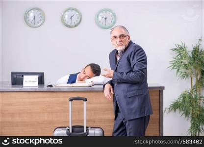 Old businessman at the hotel reception in business travel concept. Old businessman at the hotel reception