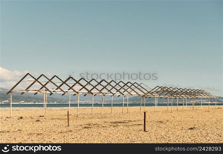 Old canopies from sun on a city pebble beach, Black Sea coast, empty calm beach on a sunny day. The sky is burnt out at noon, sea bay and in background is Caucasus mountains. Calming pastel swatches