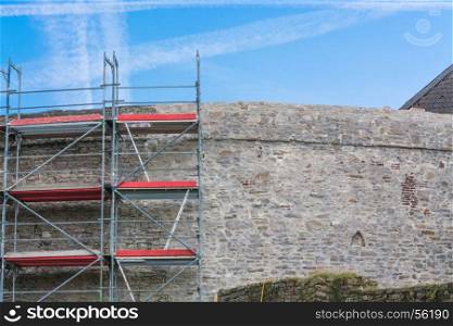 Old castle wall with scaffolding against blue sky.