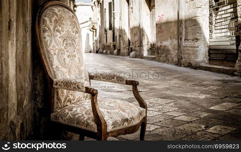 Old chair in a traditional street of Lecce, Italy.. Lecce town, Italy. Vintage chair with old town street in background.
