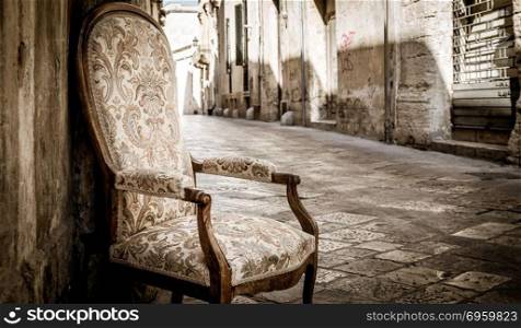 Old chair in a traditional street of Lecce, Italy.. Lecce town, Italy. Vintage chair with old town street in background.