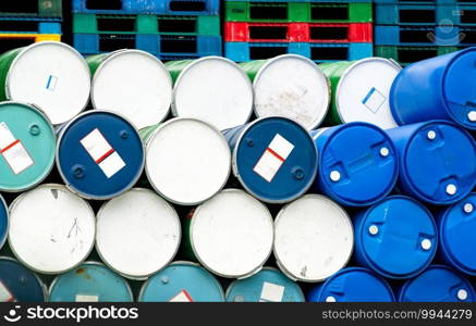 Old chemical barrels in front of stacked plastic pallet at the factory. Blue and green oil drum. Steel and plastic oil tank. Toxic waste warehouse. Hazard chemical barrel. Industrial waste in drums.