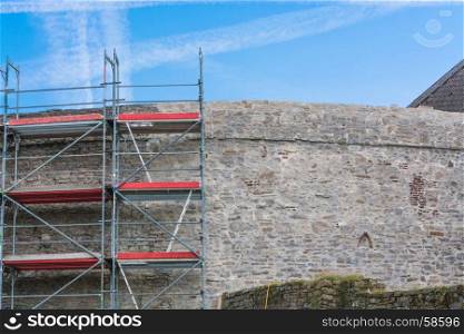Old city walls with scaffolding against blue sky.