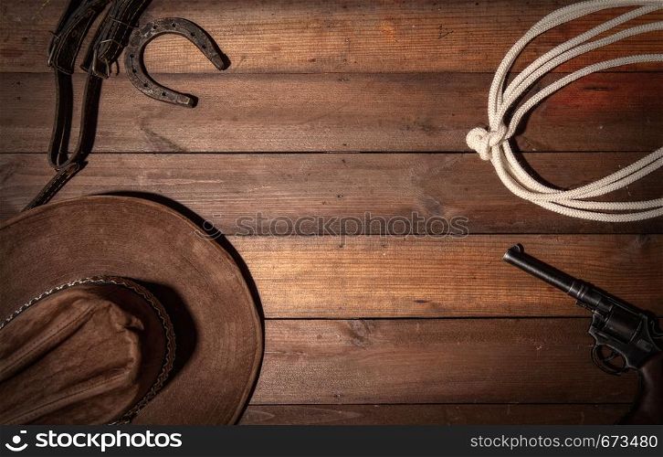 Old classic wooden background from the symphols of the cowboy wild west. Lasso, hat, revolver and horseshoe with space for text. Dark Cowboy background