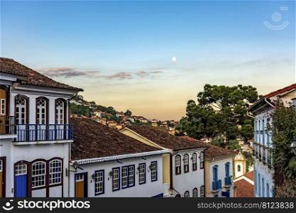 Old colonial style houses with their balconies in the traditional historic town of Ouro Preto during sunset with the moon in the background. Old colonial style houses with their balconies at dusk