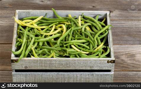 Old crate filled with freshly picked green and yellow beans on rustic wooden boards.