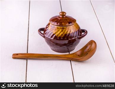 old crock pot cooking and wooden sppon on white wooden background