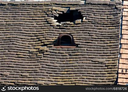 Old damaged tiled roof with broken tiles and a hole on the roof