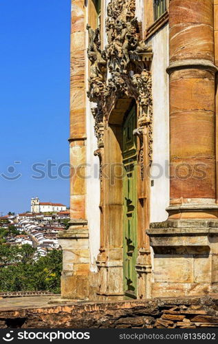 Old door and facade of historic baroque church with the city of Ouro Preto in Minas Gerais in the background. Old door and facade of historic baroque church with the city of Ouro Preto