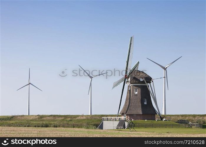 old dutch windmill and modern wind turbines against blue sky in dutch province of groningen near eemshaven in the netherlands