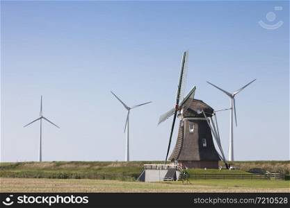 old dutch windmill and modern wind turbines against blue sky in dutch province of groningen near eemshaven in the netherlands