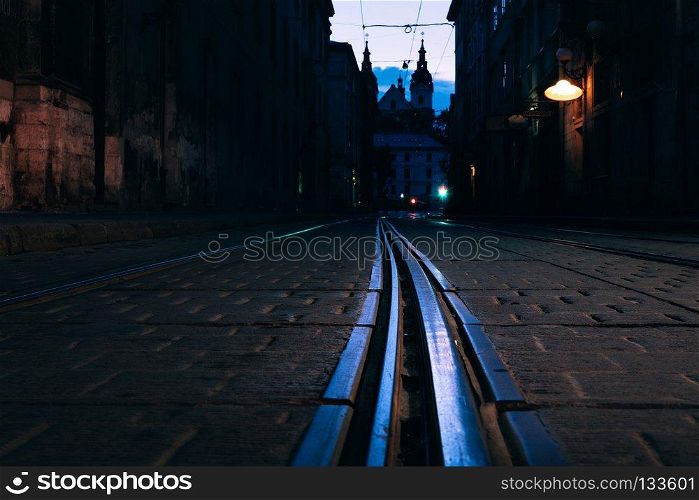 Old European city pedestrian street night city lights. Tram rails close up view. Old European city pedestrian street night city lights