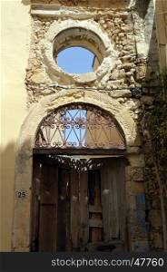 Old facade with an eye of ox, an arch with an iron motive to forge and an old wooden door.