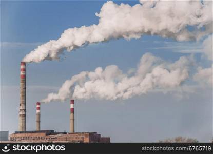Old factory chimneys with white smoke against a blue sky