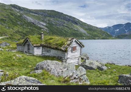old fairytale-like house of wood with chimney of stacked slate and a roof with planting and trees on a fjord in Norway with garden with red flowers and green plants near Balastrand