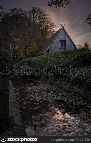 old farm in twente in the netherlands during autumn with the evening sun and a small river with waterfall in the foreground