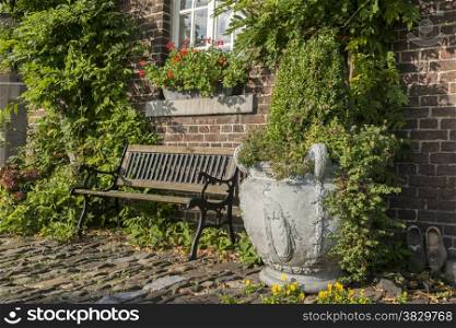 old farm with green plants on the wall and seat and vase with plants on the old rocks in the garden