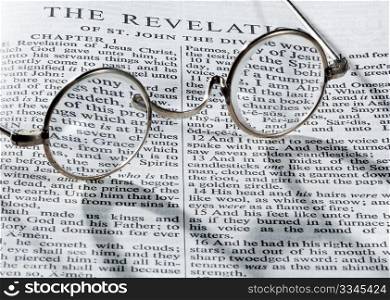 Old fashioned round reading glasses laying on a page from the bible on the revelation with strong shadow