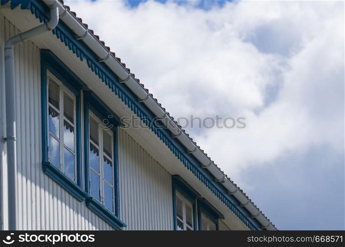 Old fashioned white wood made house with blue windows against sky with clouds. Architecture details concept.. Close up of white house with blue windows