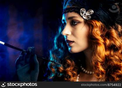Old-fashioned woman dressed in style of Flappers posing with cigarette in mouthpiece on dark background with neon light. Roaring twenties, retro, party, fashion concept. High quality photo. Old-fashioned woman dressed in style of Flappers posing with cigarette in mouthpiece on dark background with neon light. Roaring twenties, retro, party, fashion concept