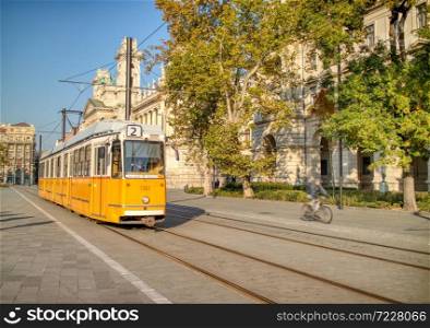 Old-fashioned yellow tram moving along historical part of city road in Budapest, Hungary in an autumn clear sunny day.. Yellow tram moving along city road in Budapest, Hungary.