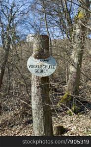 Old german sign bird sanctuary (Vogelschutzgebiet) on a tree trunk in a forest
