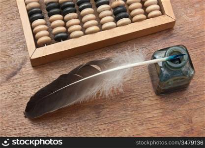 old glass inkwell with a quill pen and abacus on a wooden table