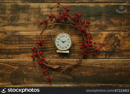 Old golden alarm clock with red berries on a wooden background