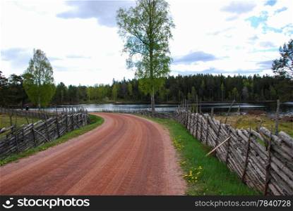 Old gravel road with tradional wooden fences by a lake at springtime. From the swedish province Smaland.