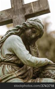 Old gravestone statue of sad thinking woman next to a cross. Sad woman gravestone