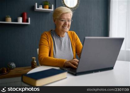 Old grey-haired woman having video conference on laptop greeting talking with children or friends. Old woman having video conference on laptop