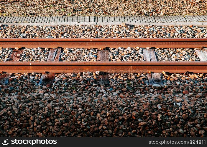 Old grungy rusty railway track with wooden crosstie and stone under sunlight with some part in shadow