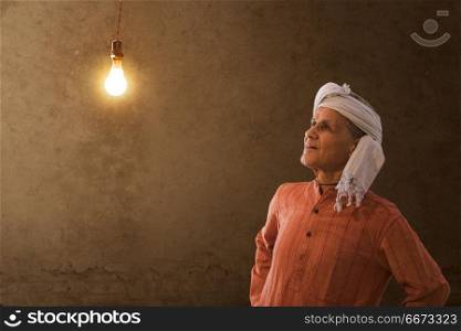 Old happy farmer looking at light bulb in his house