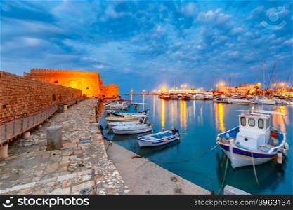 Old harbour of Heraklion with Venetian Koules Fortress, boats and marina during blue hour, Crete, Greece. Boats blurred motion on foreground.