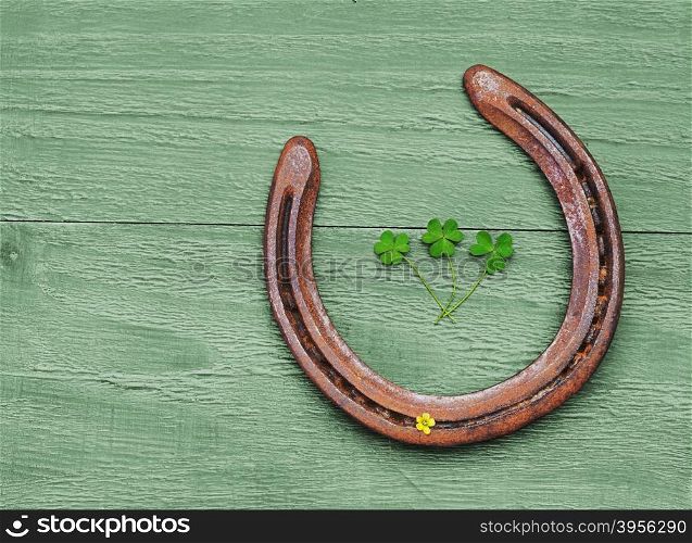 Old horseshoe and clover leaves on vintage wooden background