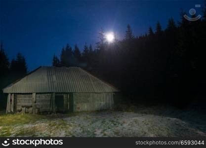 Old house in forest at night with moon light and stars on dark blue sky