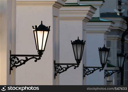 Old iron street lanterns on a white wall.. Old iron street lanterns on a white wall